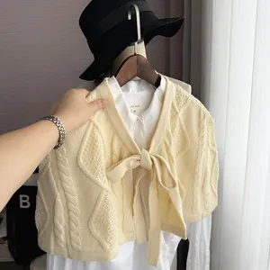 Close-up of cream knit shawl with cable-knit pattern and bow tie detail over white shirt