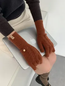 Macro detail of cable-knit wool gloves with vintage metal charm and ribbed cuffs