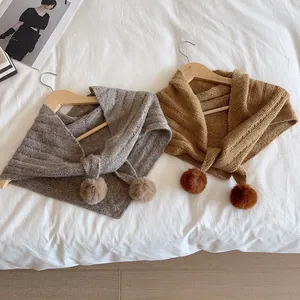 Knitted triangle shawl scarves with pom-poms in grey and caramel on a white bed