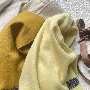 Detail of soft 100% wool scarf tassels and woven brand label in ginger and beige