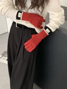 Detail of red ribbed knit gloves featuring contrast stripes and logo label on wrist