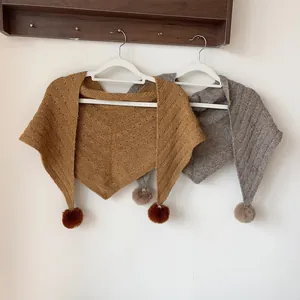 Detailed view of knitted triangle scarf with delicate hollow pattern and soft pom-poms