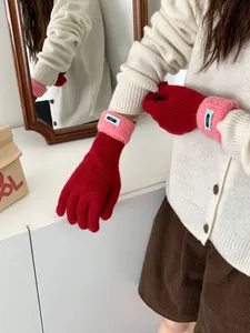 Detail von Strickhandschuhen in Rot und Rosa mit blauem Webetikett und Rollkante am Bund