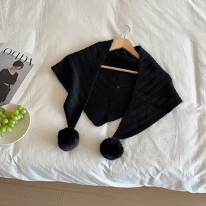 Detail of black knitted triangle scarf with soft pom-poms hanging on a wooden hanger