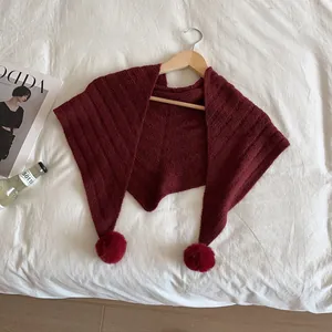 Detailed texture of burgundy knitted shawl with large soft pom-poms on wooden hanger