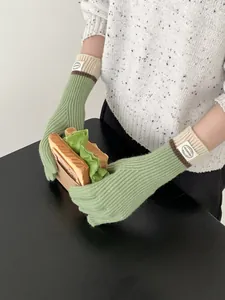 Detail of light green ribbed knit touchscreen gloves with beige cuffs on a model