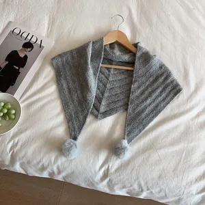 Detail of grey knitted triangle scarf with soft pom poms on a wooden hanger