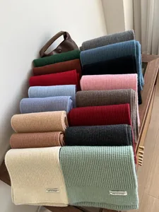 Detailansicht bunter Rippstrickschals mit weißen Webetiketten auf Holzoberfläche