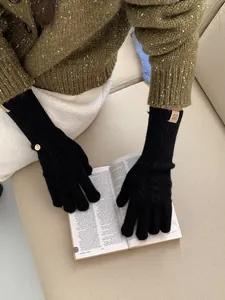 Detail of black cable knit wool gloves with leather logo patch and decorative metal tag