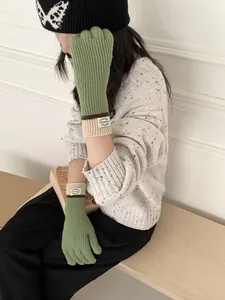 Detail of green knitted touchscreen gloves with ribbed cuffs and round fabric label