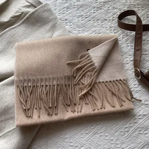 Detail shot of camel wool scarf with fringes on white knit background and beige coat