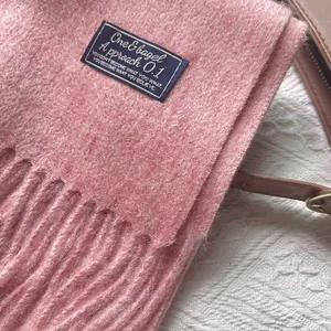 Detail of pink 100% wool scarf featuring a soft textured finish and black fabric logo label