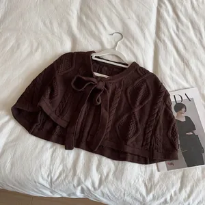 Detailed knit texture of dark brown cardigan shawl with cable stitch and bow tie