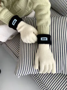 Detailansicht der cremefarbenen Strickhandschuhe mit schwarzen Rippbündchen und ERET-Label