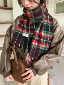 Detailed view of red and green plaid wool scarf with tassels and stitched brand label