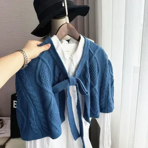 Detail of blue cable-knit short shawl featuring a front bow tie and soft cotton texture