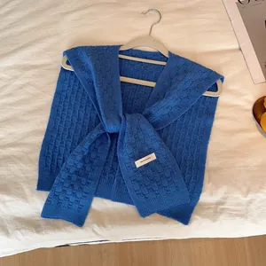 Primer plano de chal de punto azul con textura de cuadros y etiqueta de marca en percha