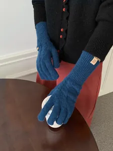 Detail of navy knit cable gloves featuring brown leather tag and wooden button closure