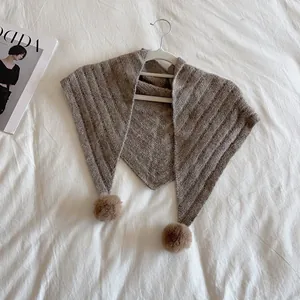 Detailed knit texture of brown shawl with soft pom-poms on a white background