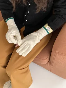 Detail of cream knit gloves featuring green stripes and a round logo patch on the wrist