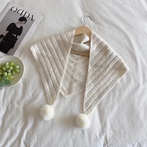 Detail of cream knit triangle shawl with soft pom-poms and vertical ribbed texture