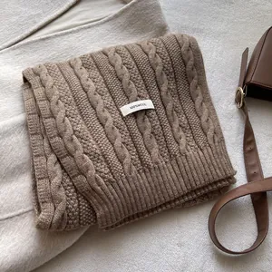 Detail showing 100% wool material label and cable knit texture of brown winter scarf
