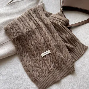 Detail of dark coffee cable knit wool scarf with a white 100% wool material label