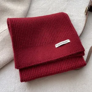 Nahaufnahme eines tiefroten Rippstrickschals mit Designetikett auf Wollstruktur