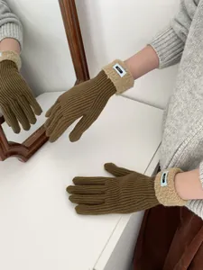 Detail von warmen braunen Strickhandschuhen mit beigen Plüschbündchen und blauem Logo-Patch