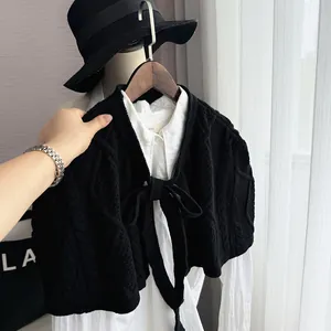 Detail of black cable-knit shawl with bow tie decoration on a white shirt