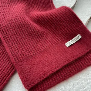 Detail eines burgunderroten Strickschals aus Wolle mit weißem Logo auf weichem Hintergrund