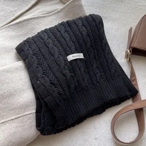 Detail of 100% wool label on black cable knit scarf with soft texture and premium weave