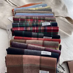 Collection of 100% wool scarves featuring classic plaid and solid patterns stacked neatly