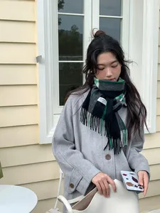 Detailed view of a green plaid cashmere scarf with fringes worn with a grey wool coat