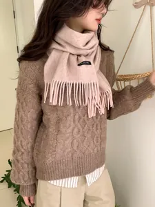 Close-up of 100% wool scarf tassel detail and fabric label on a pink scarf
