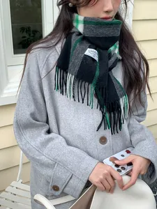 Detail of green and grey plaid cashmere scarf with soft fringe and brand label on coat