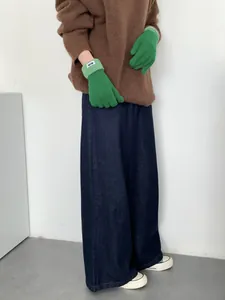 Nahaufnahme der grünen Strickhandschuhe kombiniert mit braunem Wollpullover und Jeans