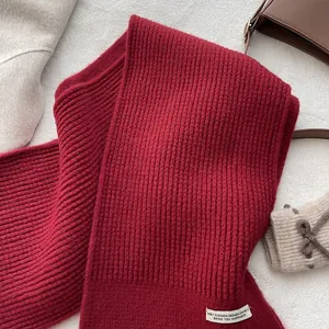 Detail eines burgunderroten Strickschals mit weißem Etikett auf grauem Filzhintergrund