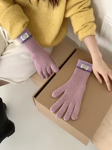 Close-up of purple ribbed knit gloves featuring a round woven brand label on the cuff