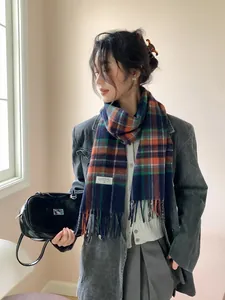 Detailed view of winter plaid wool scarf with fringe and a sewn brand label on grey coat