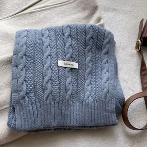 Macro detail of dusty blue cable knit wool scarf featuring an authentic 100% wool label