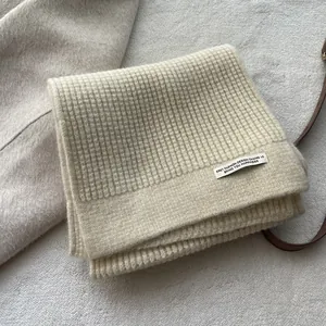 Detailaufnahme des beigen Waffelstrickschals mit Wolltextur und dezentem Markenetikett