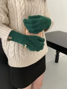 Detail of dark green cable knit gloves with a gold logo charm on a wool sweater sleeve
