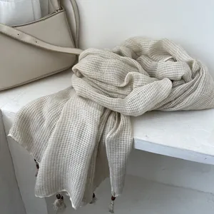 Dettaglio di sciarpa in cotone lino a quadri beige chiaro con nappe in perline di legno