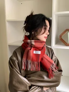 Detail of red and brown plaid cashmere scarf featuring soft fringe and stitched brand label
