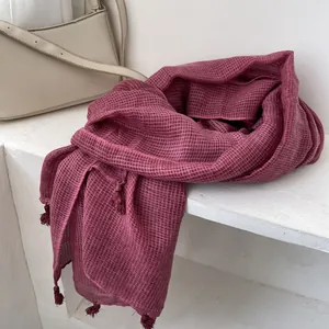Dettaglio della sciarpa in cotone e lino rosso scuro con trama a nido d'ape e nappe morbide