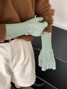 Detailed close-up of mint green wool knit glove with cable pattern and leather label