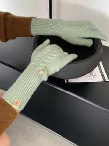 Detail of cable knit wool gloves in sage green with metal button and leather logo tag