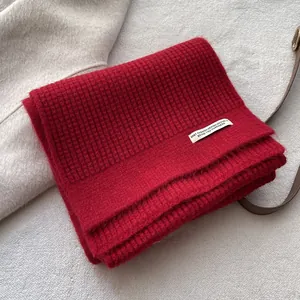Nahaufnahme eines roten Strickschals mit Waffelmuster und weißem Markenetikett