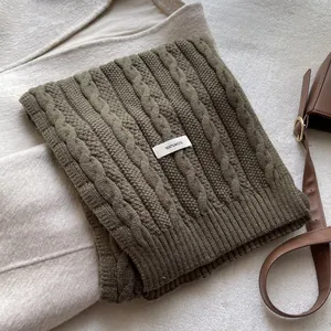Detail of dark green cable knit wool scarf featuring a 100% wool material label